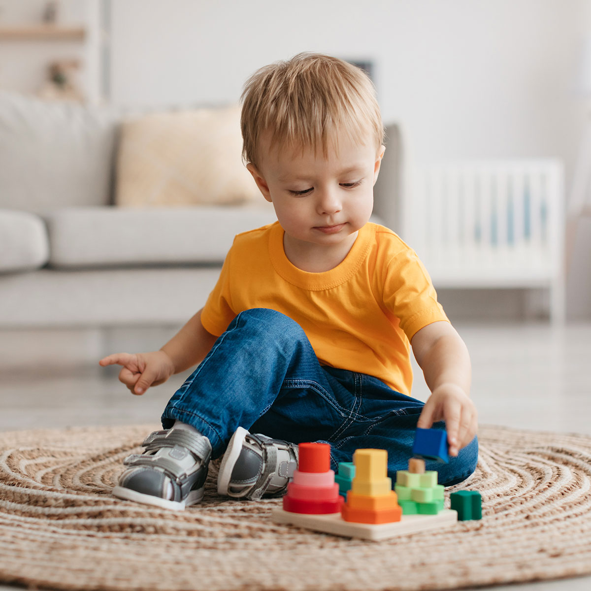 Early development concept. Little toddler boy playing with educational wooden toy at home, sitting in living room interior, free space. Child with wooden colorful stacking and sorting toy